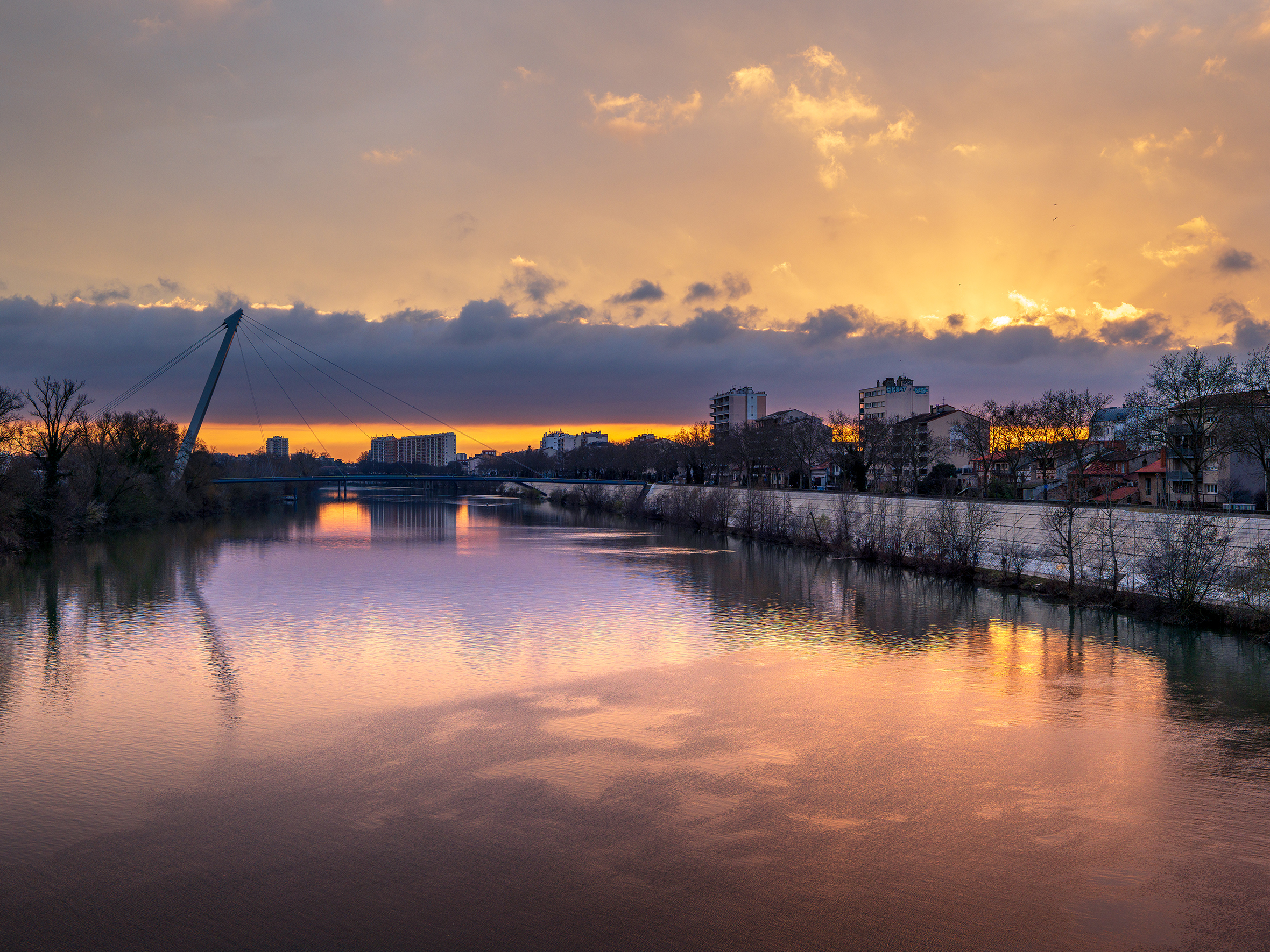 Die Garonne in Toulouse bei Sonnenuntergang mit einer Fußgängerbrücke, die von der Stadt auf die Île du Ramier führt.