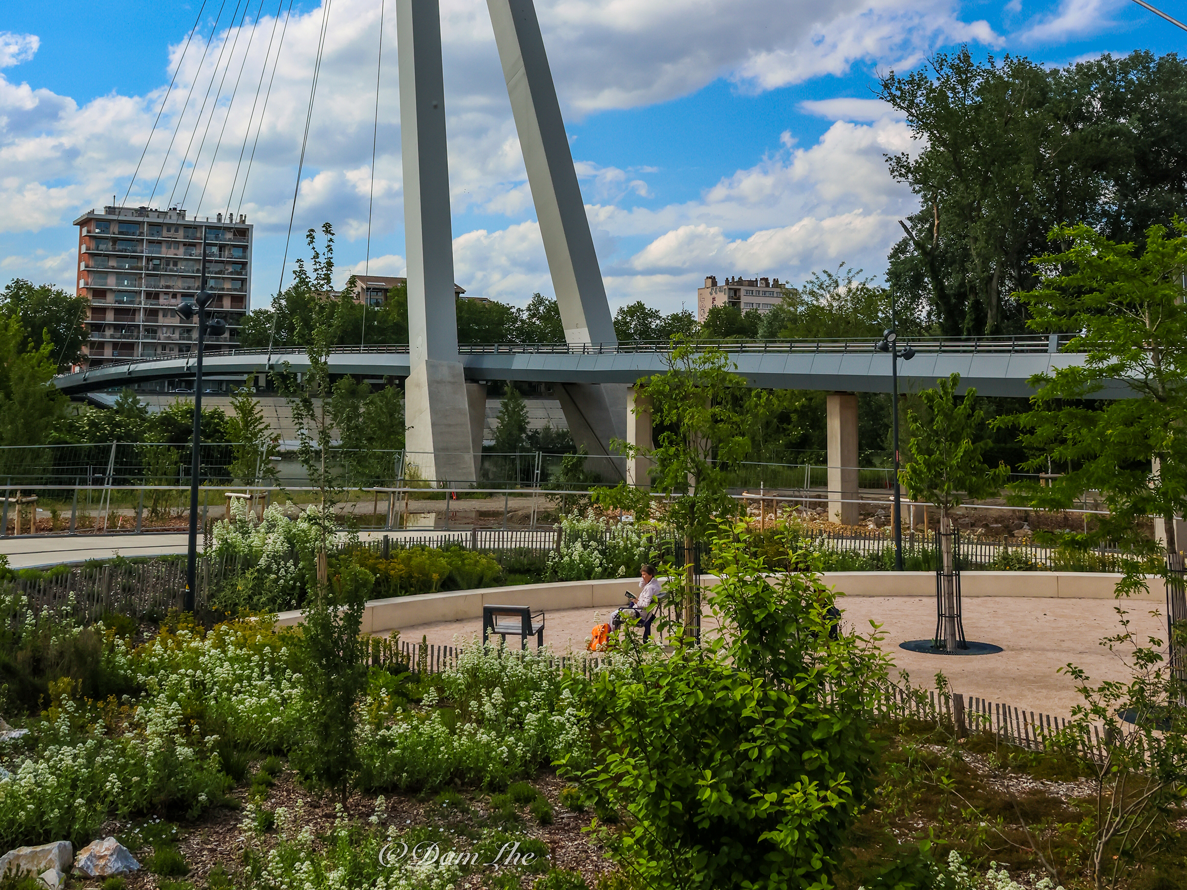 Eine Fußgängerbrücke von der Île du Ramier über die Garonne in Toulouse mit einem begrünten Platz im Vordergrund.