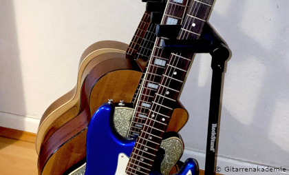 Mehrer Gitarren stehen hintereinander in einem Ständer.