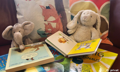 Zwei Kuscheltiere sitzen mit aufgeschlagenen Bilderbüchern auf und vor Stoffkissen.