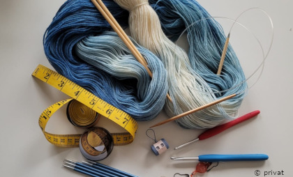 Foto mit blauer Wolle und verschiedenen Strick- und Häkelnadeln