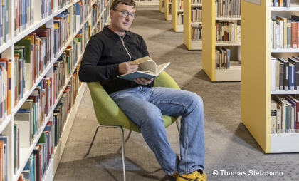 Foto von einem Mann, der in der Bibliothek auf einem Sessel sitzt für die  Ausstellung "Menschen im KAP1"