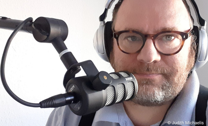 Ein Mann sitzt mit Kopfhörern vor einem Podcastmikrofon