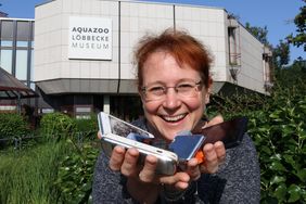 Die stellvertretende Direktorin des Aquazoo, Sandra Honigs, steht vor dem Institut und hält defekte Smartphones und leere Druckerpatronen in den Händen