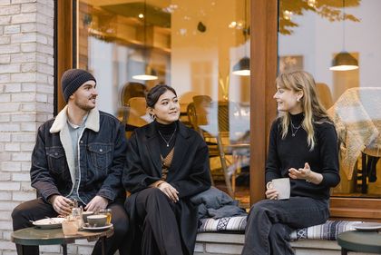 Drei junge Menschen trinken Kaffee vor einem Lokal
