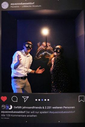 Ein Mann und eine Frau stehen mit Tauchermasken bekleidet in der Instabox. Hinter den beiden Personen ist das Bild eines Tiefsee-Anglerfisches zu sehen.