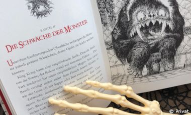 Foto mit Blick auf ein aufgeschlagenes Buch mit Monstergeschichten und eine Skeletthand, die die Seite blättert.