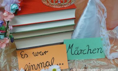 Foto mit Märchendekoration und einem Bücherstapel mit bunten Zetteln, auf denen "Es war einmal..." und "Märchen" steht.