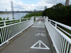 Um die Hafeneinfahrtsbrücke, besonders für Radfahrer, sicherer zu machen, wurden die Geländer des Brückenbauwerkes optimiert und die Bodensohle angepasst. Markierungen auf der Fahrbahn signalisieren jetzt "Achtung Radverkehr Langsam" © Landeshauptstadt Düsseldorf, Amt für Verkehrsmanagement 