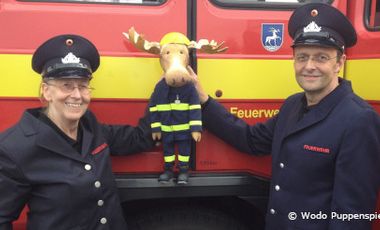 Foto mit den Puppenspielern von Wodo Puppenspiel und der Handpuppe Finn, der Feuerwehrelch vor einem Feuerwehrauto.