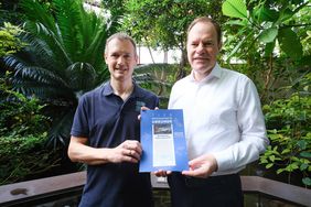 OB Dr. Stephan Keller (r.) erhielt von Aquazoodirektor Dr. Jochen Reiter die Patenschaftsurkunde für das Süßwasserkrokodil "Old Lady". Reiter trägt ein blaues Polohemd und blick tin die Kamera. Er überreicht Herrn Dr. Keller links neben sich die blaue Patenschaftsurkunde, auf der ein Foto des Patentiers abgebildet ist. Auch Herr Dr. Keller im weißen Hemd schaut in die Kamera.