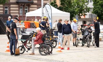 Foto vom Beratungsstand des TEst-Events mit einer Gruppe von Menschen die sich in der Beratung befinden und teilweise auf Spezialrädern sitzen.