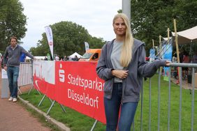 Zwei Mitarbeitende (Frau im Vordergrund, Mann im Hintergrund)flankieren ein Banner der Stadtsparkasse Düsseldorf am Eingang zum Familienfest 