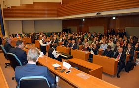 Blick vom besetzten Podium ins Publikum, dazwischen spielen ein Geiger und ein Pianist