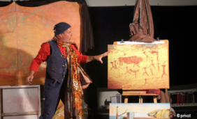Foto von Theater Tom Teuer: ein Mann steht mit Bildern auf der Bühne