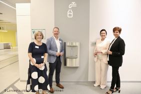 Foto von vier Personen am neuen Wasserspender in der Zentralbibliothek. Zu sehen sind vlnr: Martina Leschner, Leitung Zentralbibliothek, Stephan Schwering, Direktor der Stadtbüchereien Düsseldorf, Miriam Koch, Dezernentin für Kultur, Migration und Gesundheit und Tatiana Helfrich von der Stiftung Nachhaltigkeit der Stadtsparkasse