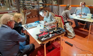 Menschen sitzen mit Werkzeug an Tischen und repaieren Kleingeräte
