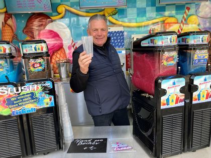 Schausteller Max Cronenberg hält stolz einen Mehrwegbecher hoch