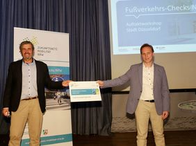 Michael Zyweck (Zukunftsnetz Mobilität NRW) überreichte die Urkunde für die Teilnahme an den Fußverkehrs-Checks 2020 an Florian Reeh (Amts für Verkehrsmanagement). Foto: Lammert