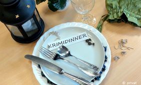 Foto von einem Geschirrgedeck mit Besteck, Schmuck, einem Glas und dem Schriftzug "Krimidinner"