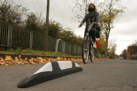 Bild von einem Trennelement der Protected Bike Lane und einer Radfahrerin im Hintergrund.