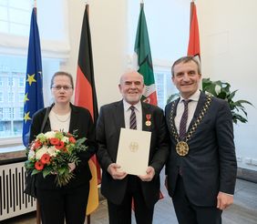 Der mit der Bundesverdienstmedaille ausgezeichnete Wilhelm Mayer (Mitte) mit seiner Frau Natalja Mayer-Karassjova (links) und Oberbürgermeister Thomas Geisel beim Empfang im Rathaus. Foto: Michael Gstettenbauer